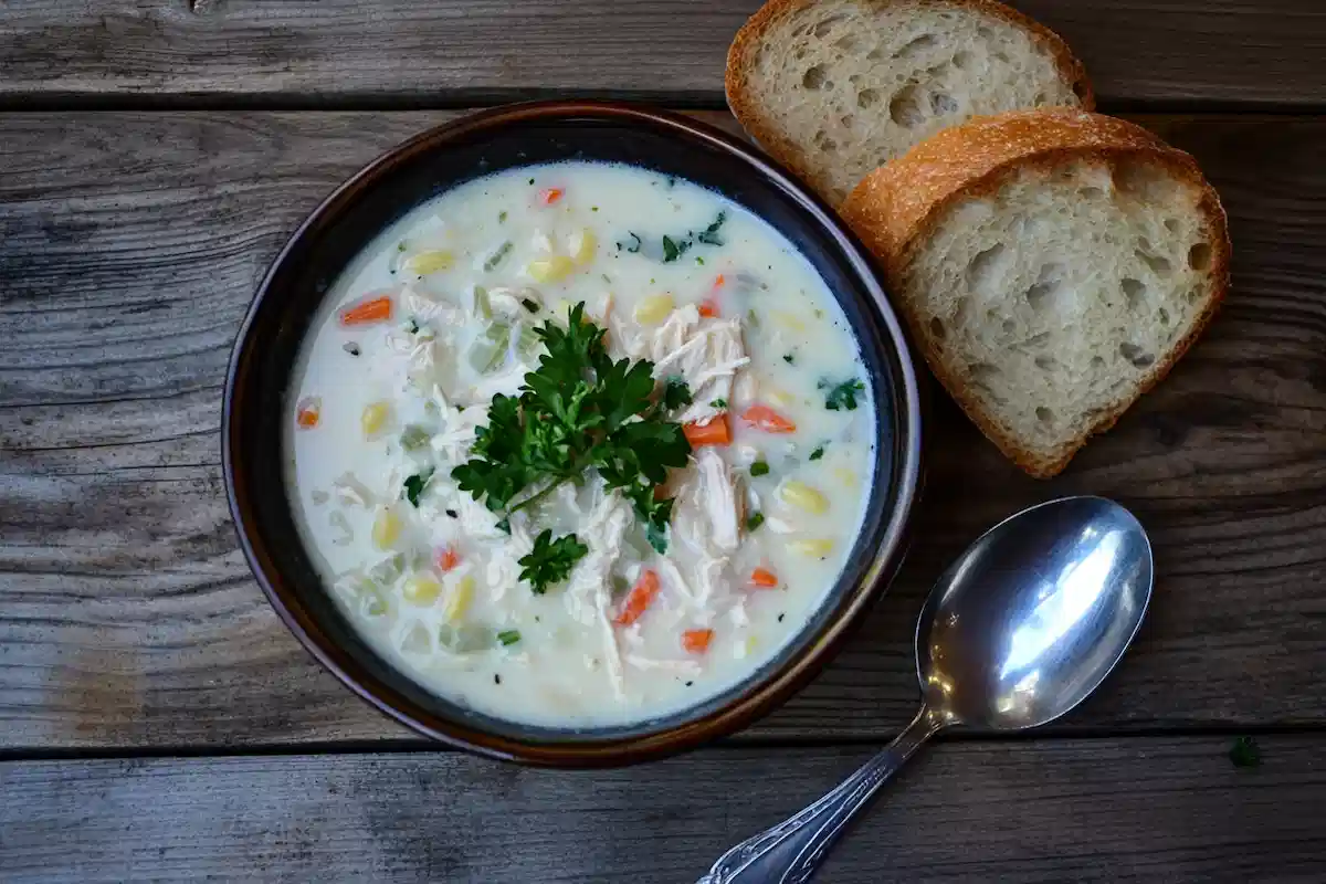 Bowl of creamy classic chicken noodle soup with shredded chicken, vegetables, and fresh parsley served with bread