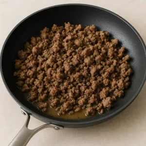 Ground beef cooking in a black non-stick skillet with rendered fat.