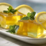 Lemon honey gelatin cubes on white plate with fresh lemon slices and mint garnish