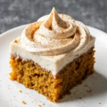 A perfectly soft pumpkin bar with thick cream cheese frosting on a white plate, showing the moist crumb texture.