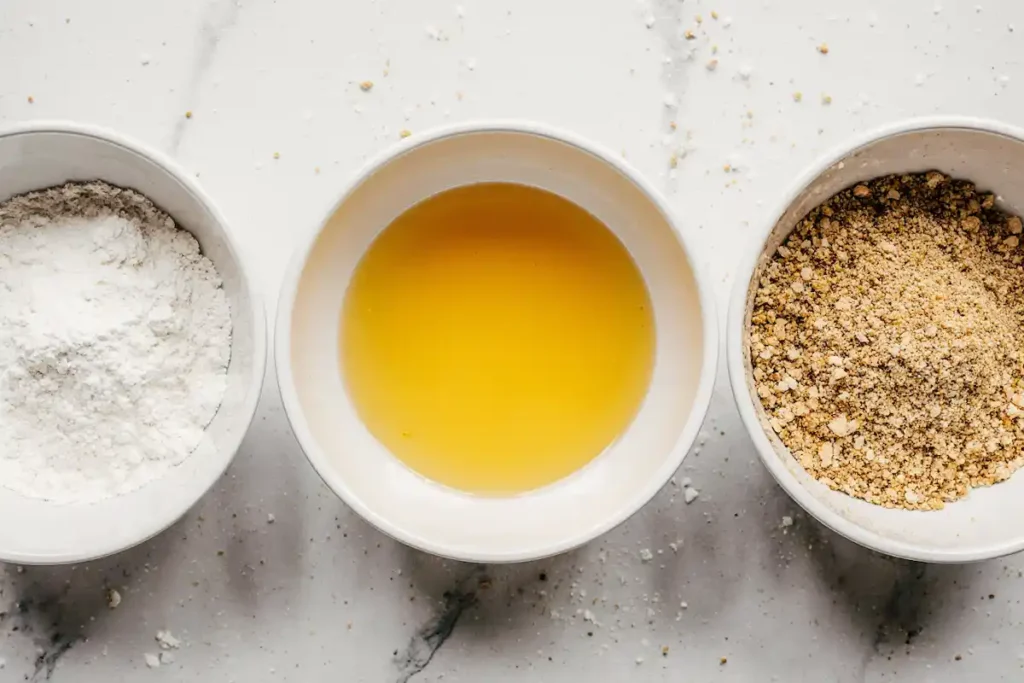 hot-honey-feta-chicken-recipe-breading-tutorial-steps Hot honey feta chicken recipe breading process with flour, egg, and panko breadcrumbs in bowls