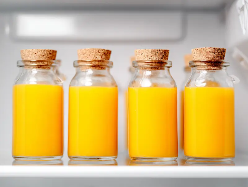 Four lemon ginger cayenne shots stored in small glass bottles with cork tops on white refrigerator shelf for meal prep