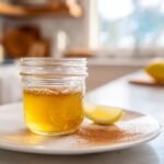 Close-up of the Ben Carson honey recipe in a small glass jar on a white plate with cinnamon and lemon.