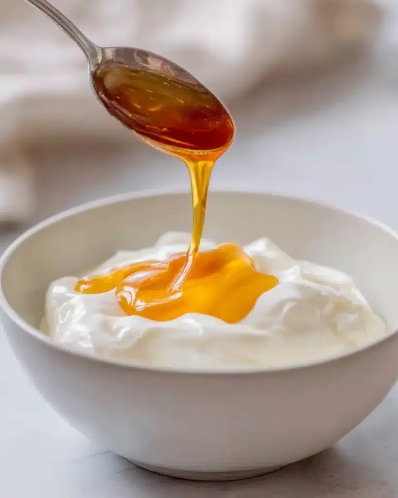 Ben-Carson-Honey-Recipe-Yogurt-Serving Ben Carson honey recipe drizzled over plain yogurt in a white bowl.