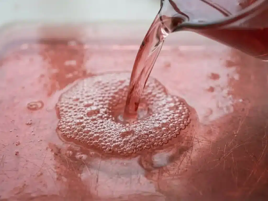 Dr William Li Gelatin Recipe: 3 Ingredients, Real Results 15 pink gelatin liquid being poured mid-stream from measuring cup into rectangular glass dish for dr william li gelatin recipe for weight loss step 4